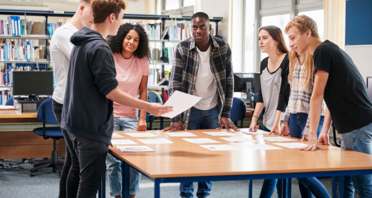 College students standing around a table discussing ideas.