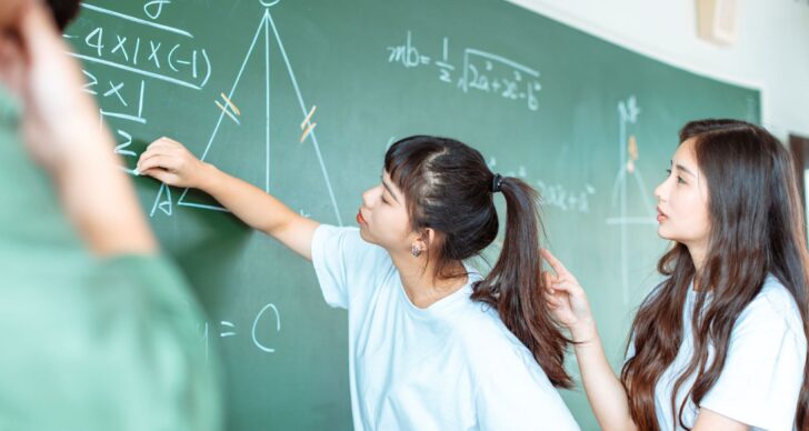 Two A Level students doing maths calculations on a blackboard